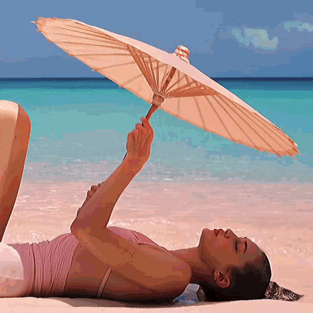 a woman is laying on the beach holding an umbrella over her head