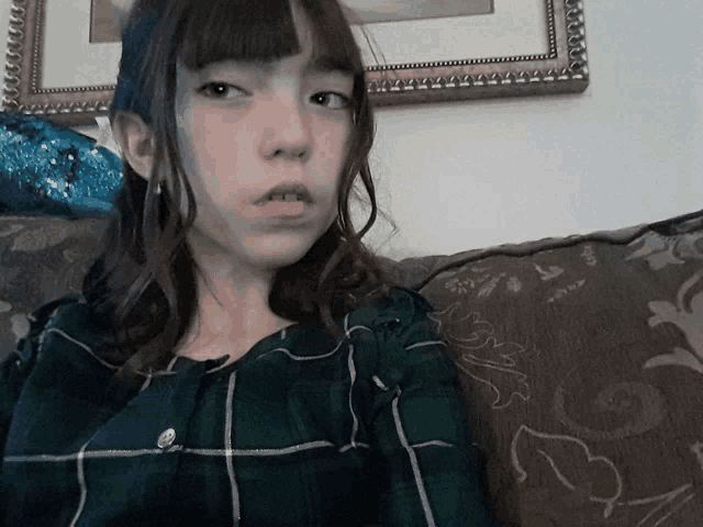 a girl in a plaid shirt sits on a couch in front of a picture frame
