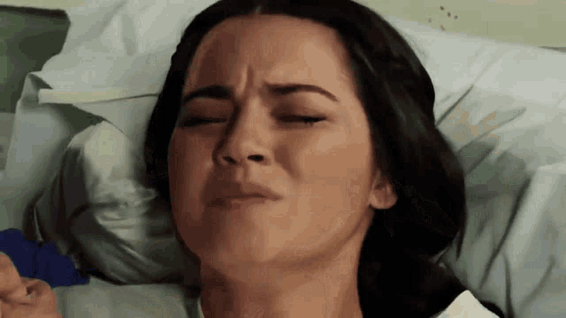 a woman is laying in a hospital bed with her eyes closed and a sad look on her face