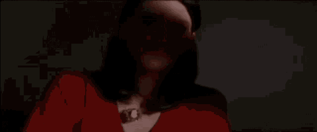a man with long hair and a red shirt is smiling in a dark room with the word wife behind him .