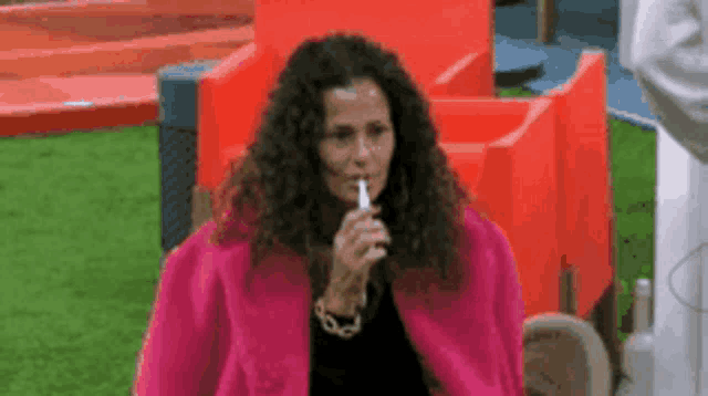 a woman in a pink coat is smoking a cigarette while sitting in a chair .