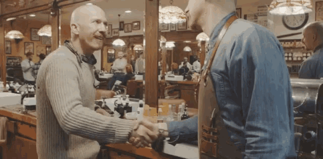two men shaking hands in a barber shop with one wearing a blue shirt