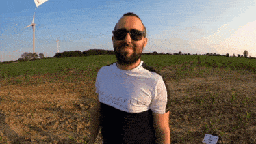a man wearing sunglasses and a los angeles t-shirt stands in a field