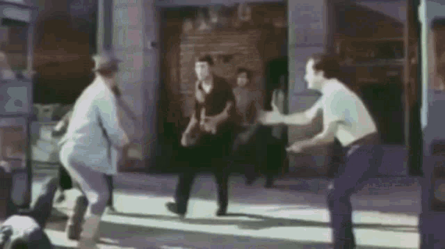 a group of men are standing on a sidewalk in front of a building and fighting each other .
