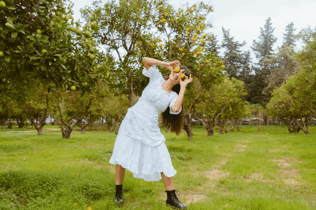 a woman in a white dress is standing in a field with trees