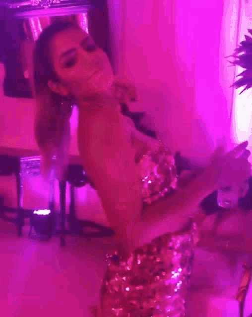 a woman in a sequined dress is dancing in a room with pink lighting .