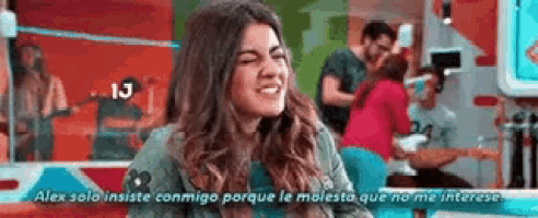 a woman is making a funny face in front of a group of people in a room while talking to a man .