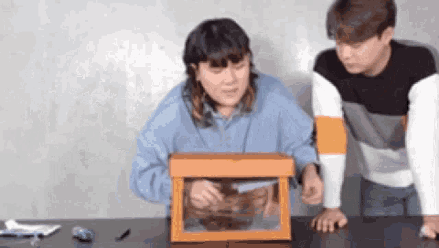a man and a woman are sitting at a table looking at a box with a toy in it .