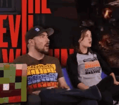a man and a woman sit on a couch in front of a sign that says " evil "