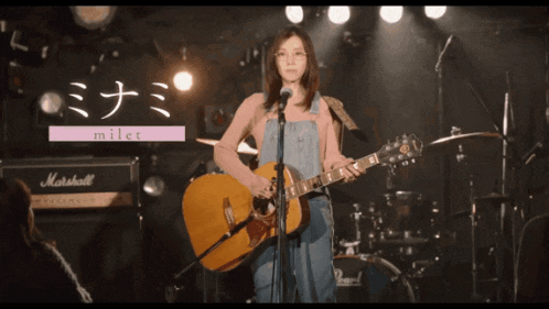 a woman singing into a microphone while holding a guitar with a marshall amp in the background