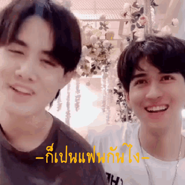two young men are standing next to each other and smiling in front of a flower arrangement .