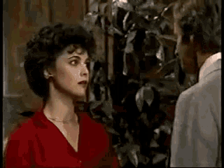 a man and a woman are looking at each other in a room . the woman is wearing a red dress .