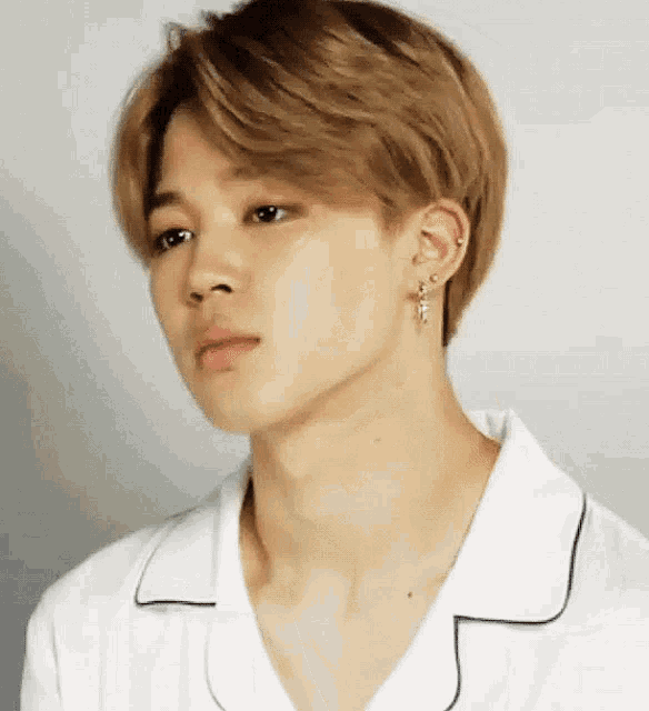 a young man wearing a white shirt and earrings is looking at the camera .