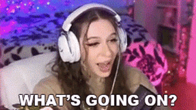 a woman wearing headphones is sitting on a bed and looking at a phone .