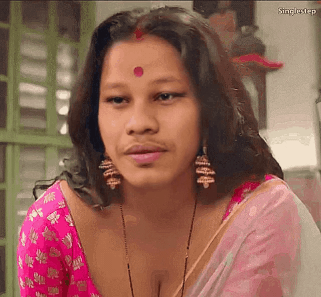 a woman wearing a pink top and earrings looks at the camera