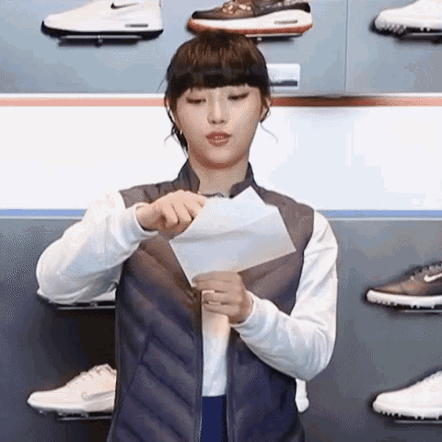 a woman is holding a piece of paper in front of a wall of shoes