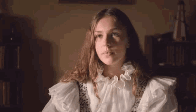 a young girl in a white dress is sitting at a table in a dark room .