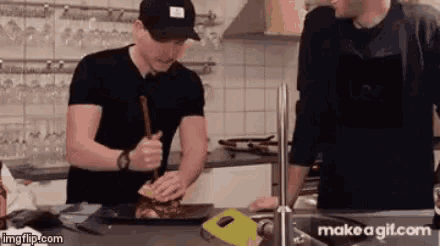 two men are preparing food in a kitchen and one of them is wearing a hat