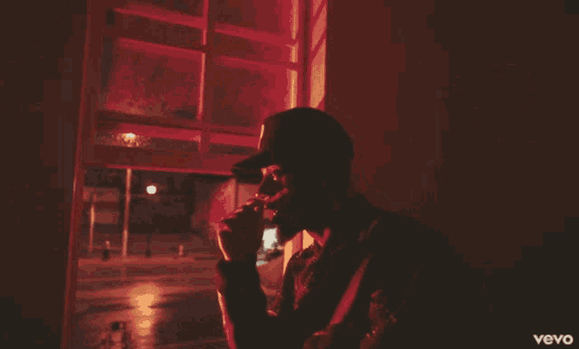 a man smoking a cigarette in a dark room with a vevo logo on the bottom