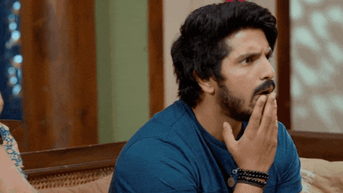 a man with a beard wearing a blue shirt is covering his mouth with his hand