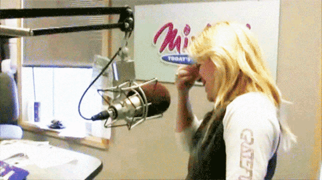 a woman stands in front of a microphone in front of a sign that says " mi today "