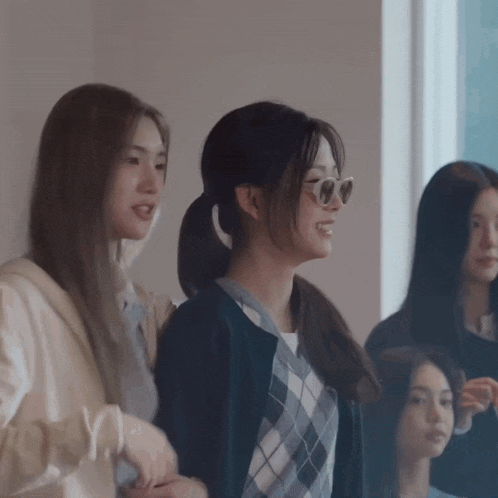 a group of young women are standing in front of a window and smiling .