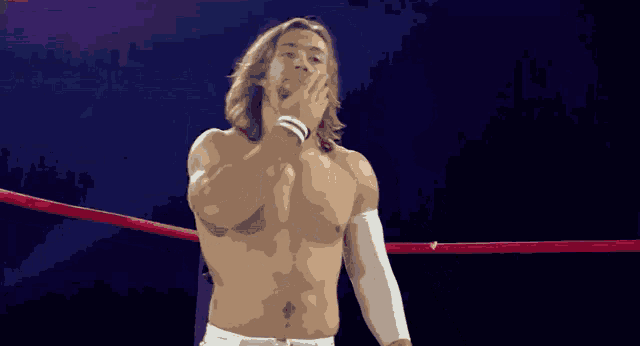 a shirtless wrestler stands in a ring with his hands on his chest