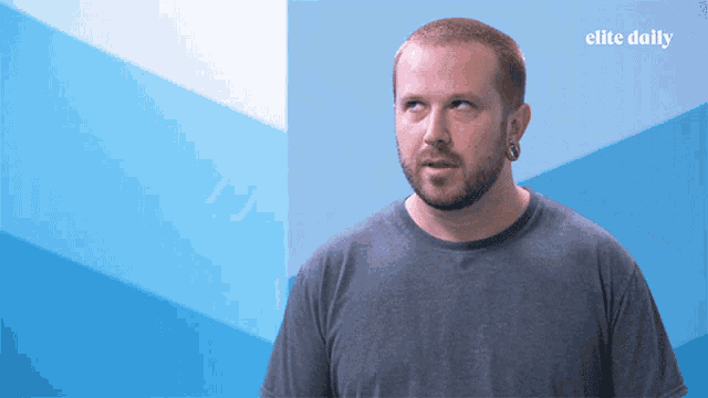 a man stands in front of a blue wall with elite daily written on the bottom