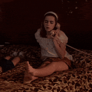 a young girl is sitting on a bed talking on a phone