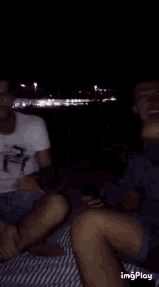 two men are sitting next to each other on a picnic blanket at night .