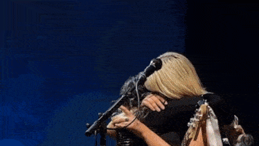 a woman is drinking water from a bottle while singing into a microphone on a stage .