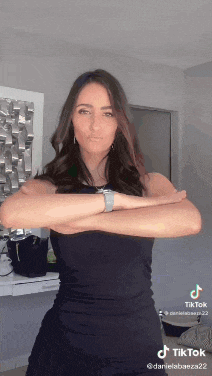 a woman in a black dress is standing with her arms crossed in a room .