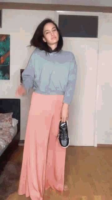 a woman in a blue sweatshirt and pink pants is holding a pair of sneakers .