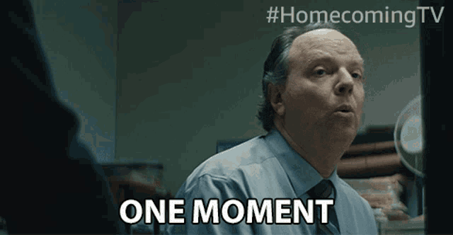 a man says " one moment " in front of a sign that says homecoming tv