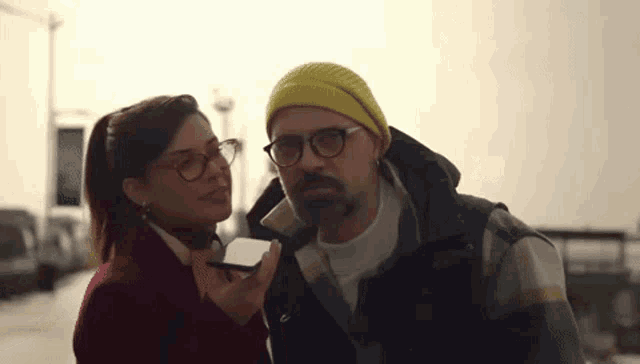 a man and a woman are standing next to each other and the woman is holding a cell phone .