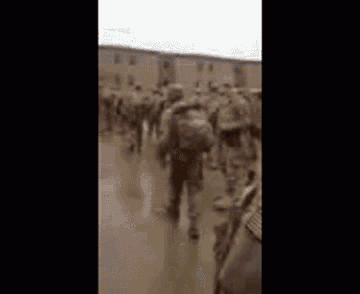 a group of soldiers are marching down a muddy street in front of a building .