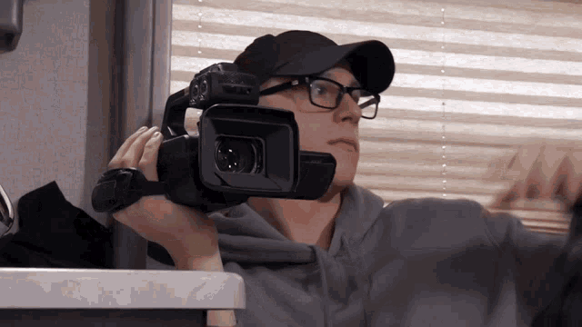 a man wearing glasses and a hat holds a camera