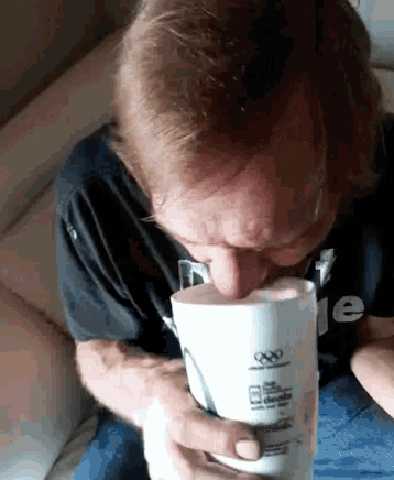 a man in a black shirt is drinking from a cup that says ' olympic ' on it