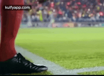 a soccer player wearing red socks and black shoes is standing on the sidelines of a soccer field .