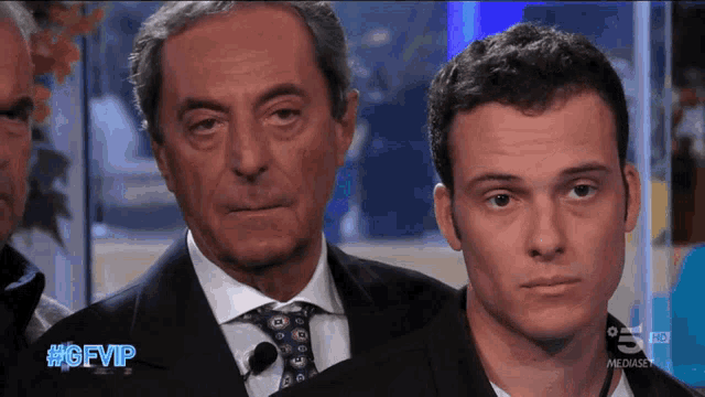 a man in a suit and tie stands next to a younger man with the caption #gfvip on the screen