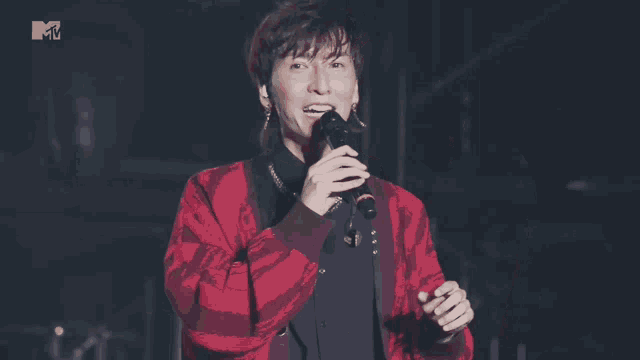a man in a red jacket singing into a microphone with a mtv logo behind him