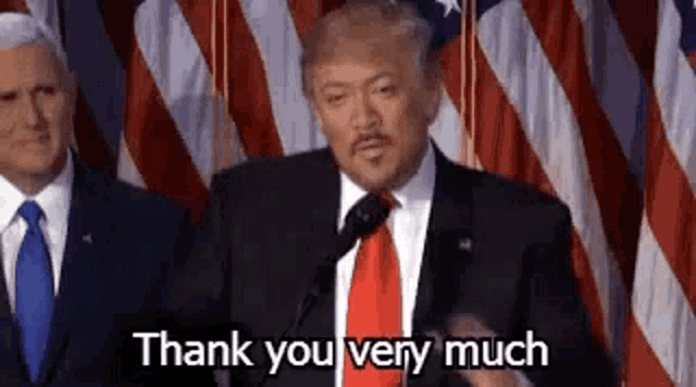 a man in a suit and tie is giving a speech in front of an american flag .