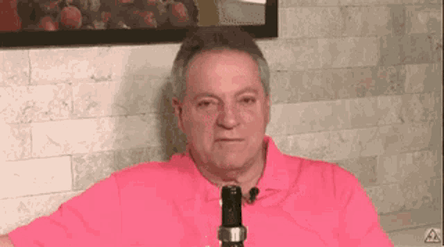 a man in a pink shirt is sitting in front of a brick wall holding a wine bottle .