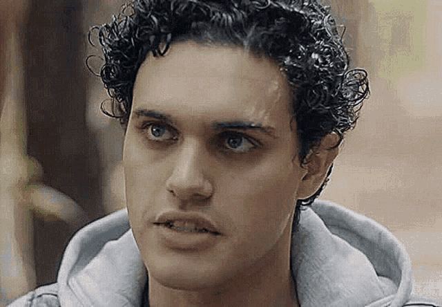 a close up of a man 's face with curly hair wearing a grey hoodie .