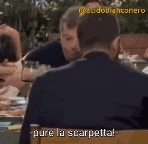 two men are sitting at a table and one of them says -pure la scarpetta