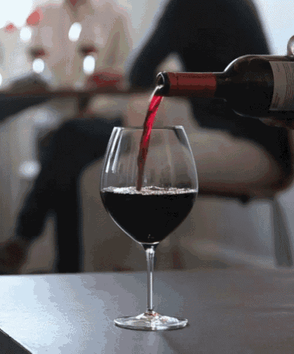 a glass of red wine is being poured from a bottle on a table