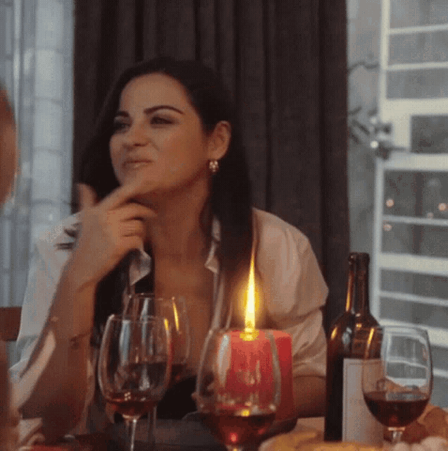 a woman sits at a table with a bottle of wine and glasses of wine