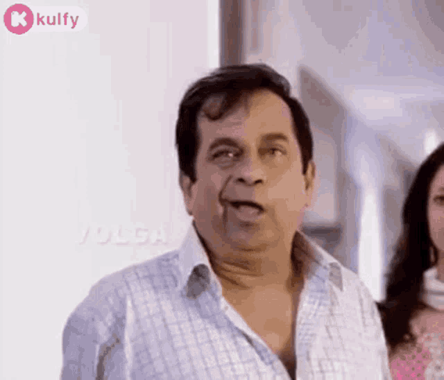a man in a plaid shirt is making a funny face while standing next to a woman in a pink dress .