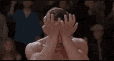 a man with blood on his face is standing in a boxing ring with his hands in the air .