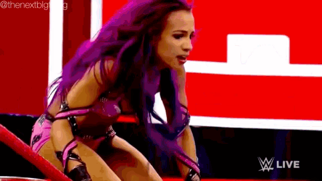 a female wrestler with purple hair is sitting on a red ring .